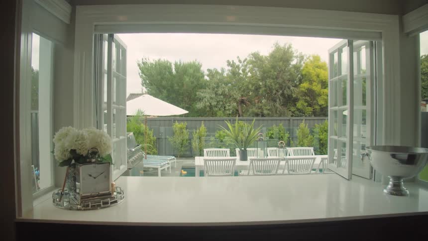 The view from a kitchen in a house of a backyard with a table and swimming pool