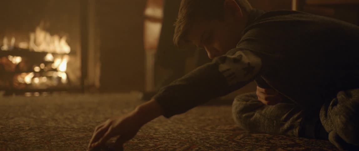 A boy pushes a toy car around in front of the fireplace