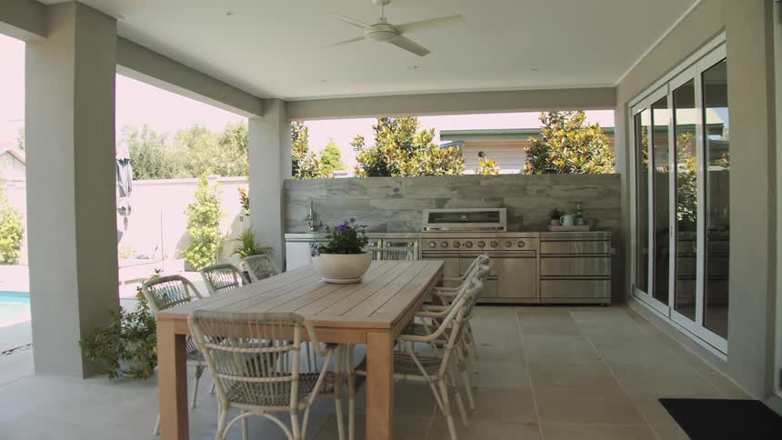 An outdoor kitchen and table sit on the back porch of a home with a pool
