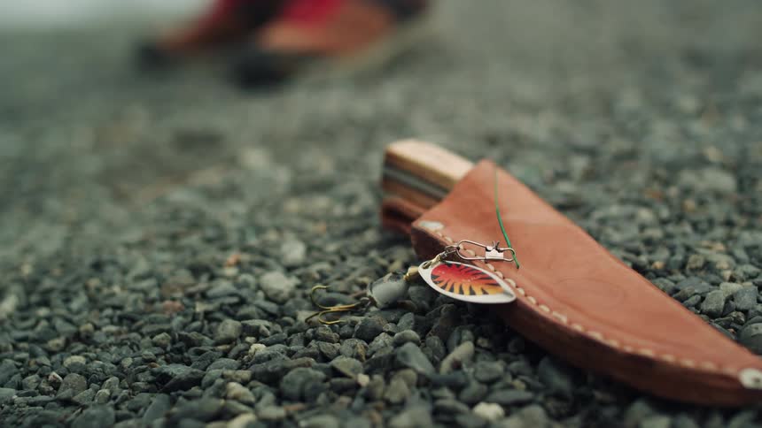 A leather sheath with wooden knife handle sticking out lies on rocky ground