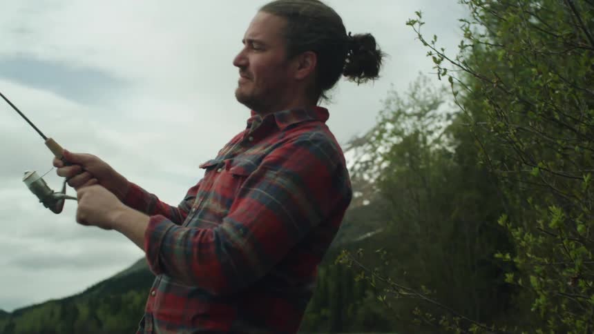Man uses a fishing rod on a lake near the mountains