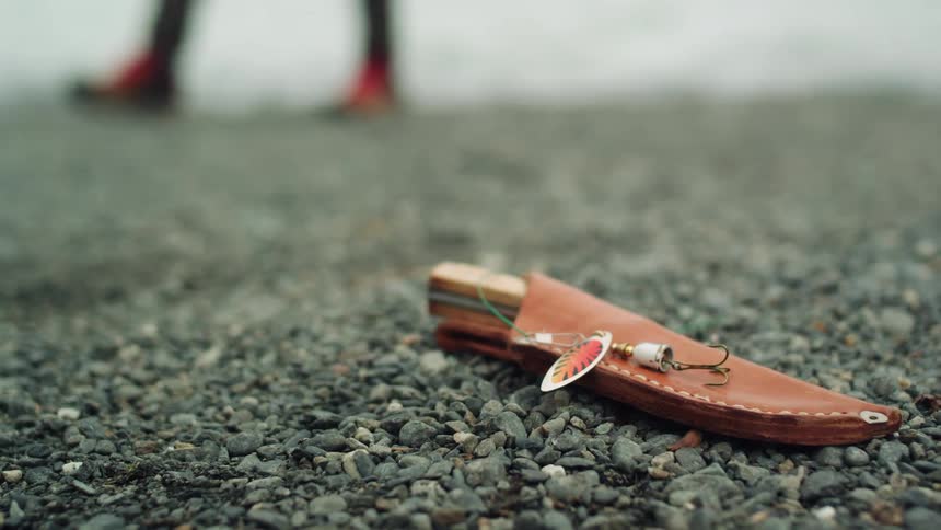 A knife is on the ground on the gravel as a person walks by