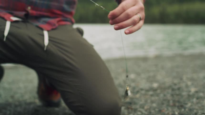 Man with brown pants red plaid shirt prepares fishing line to cast