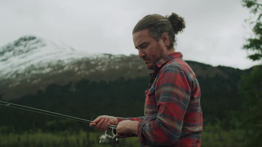 Man with long hair and red plaid shirt fishes in the lake