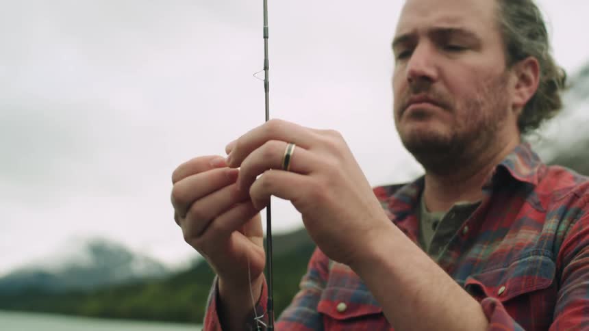 Man threading a fishing rod next to a lake in the mountains