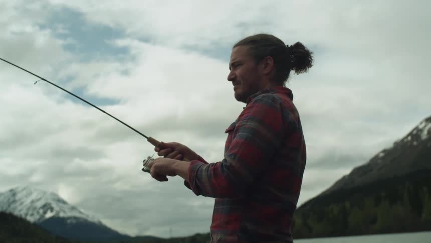 Young man fishing on a lake near the snow covered mountains