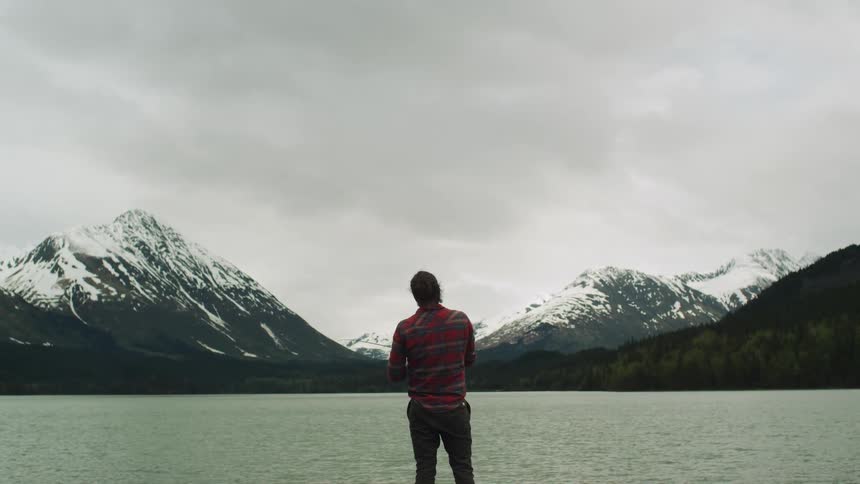 A man fishes on a lake in front of a mountain range