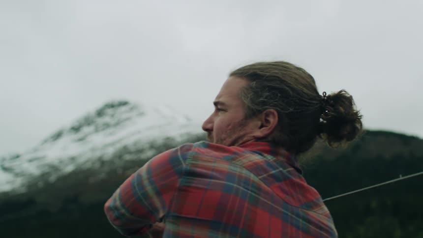 Man with long hair and plaid shirt casts a fishing line