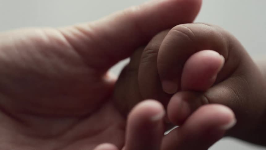A parent lovingly holds and caresses a babys hand