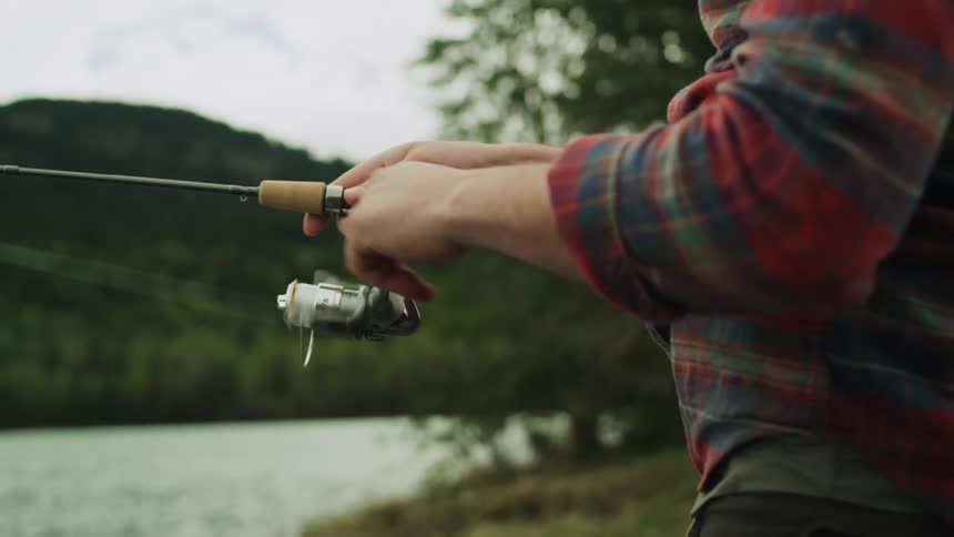 A man is reeling in his fishing rod by the lake