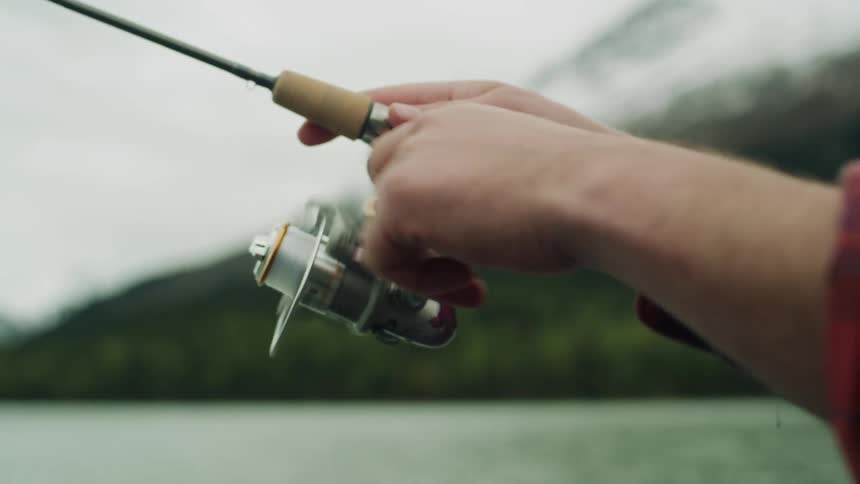 A man turns the reel on his rod as he fishes in a mountain lake