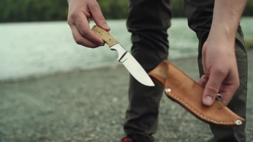 A man unsheathes a hunting knife and puts it back after examining it