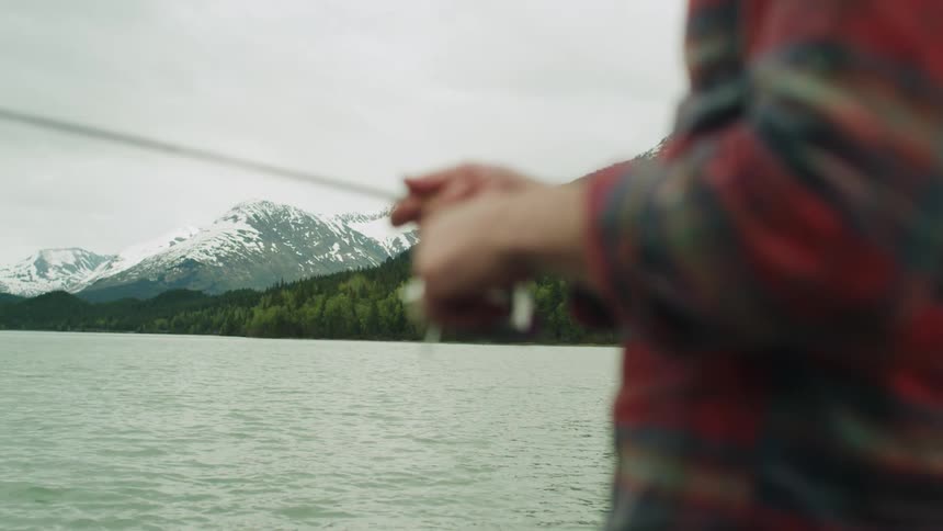 A man turns the reel on his rod as he fishes in a mountain lake