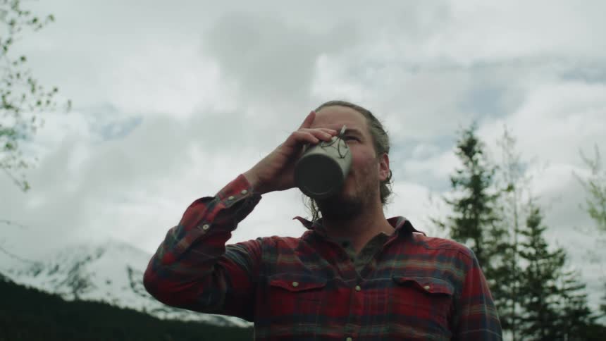 Man drinking from a metallic cup near the snow covered mountain tops