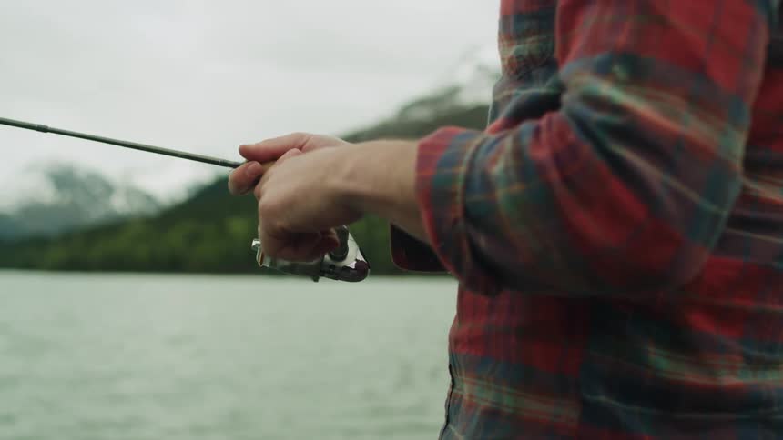 A man reels in his fishing rod while fishing in a lake