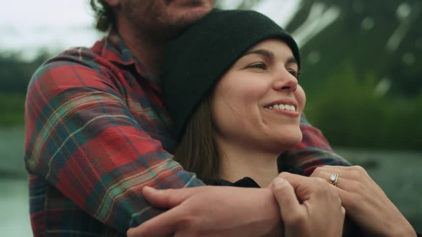 A woman is hugged from behind by a man while standing in the wilderness during the day