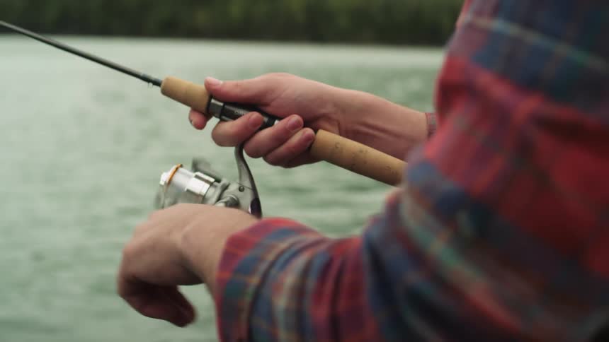 A man turns the reel on his rod as he fishes in a lake