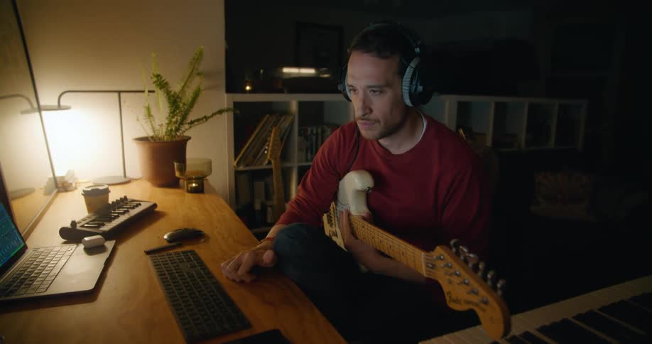 A man is listening to music then playing on his guitar