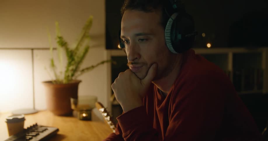 Man with headphones and red sweater listens to music and looks at desktop