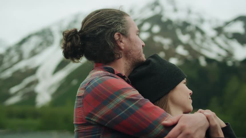 A man and a woman are hugging with snow clad mountain visible in the background