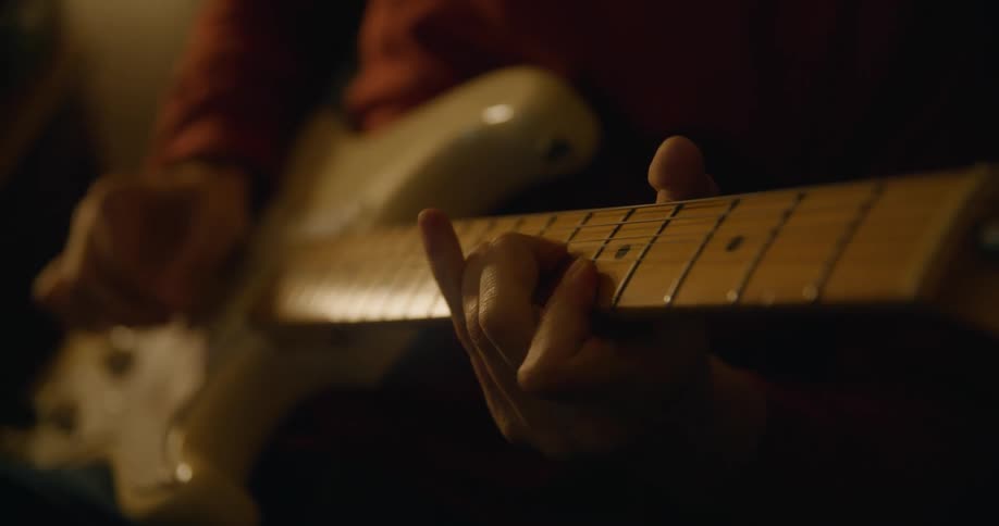Person playing with an electric guitar inside a dimly lit room