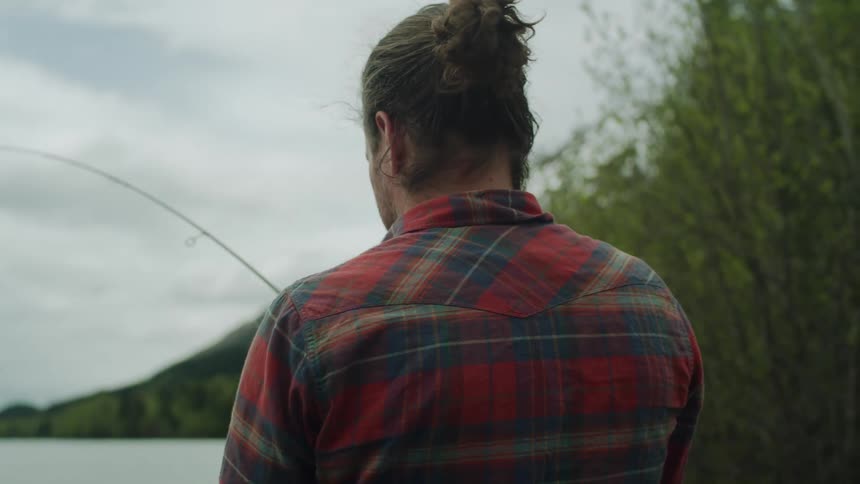 A man stands on the shore and pulls on his fishing rod as he fishes