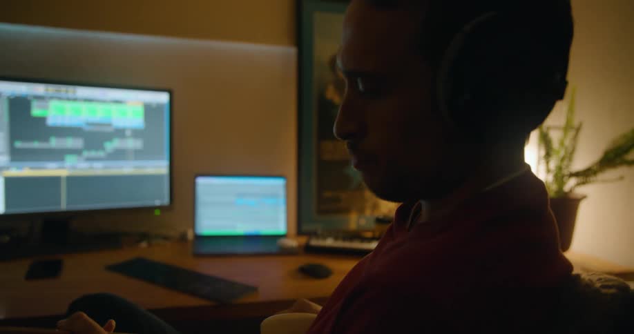 Man with headphones and red sweater strums bass guitar in studio