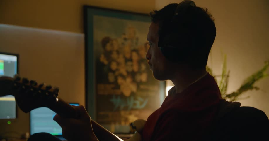 A man uses a laptop and computer to record himself playing guitar at home