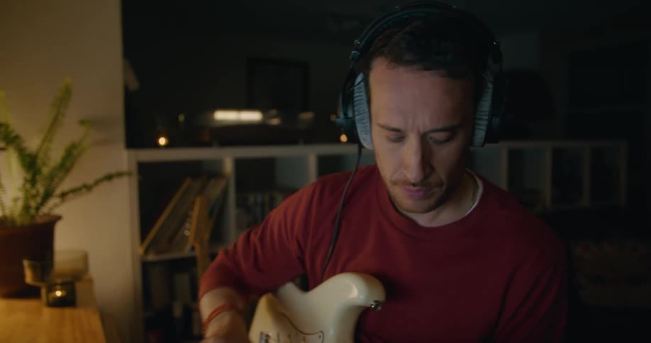 Man sits in chair in dimly lit room playing guitar