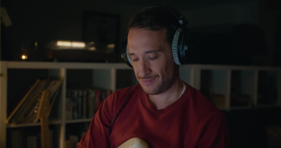 Young man wearing headphones texting on the phone while holding an electric guitar