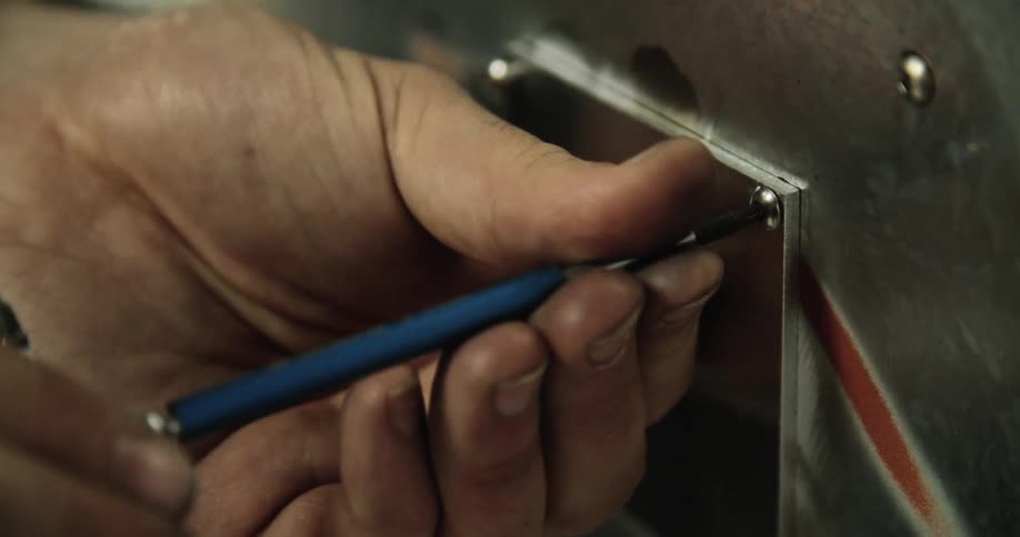 A person screwing in a screw on a metal plate