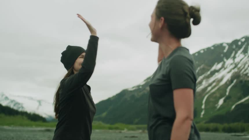 Two women near snowy mountains are laughing and giving a high five