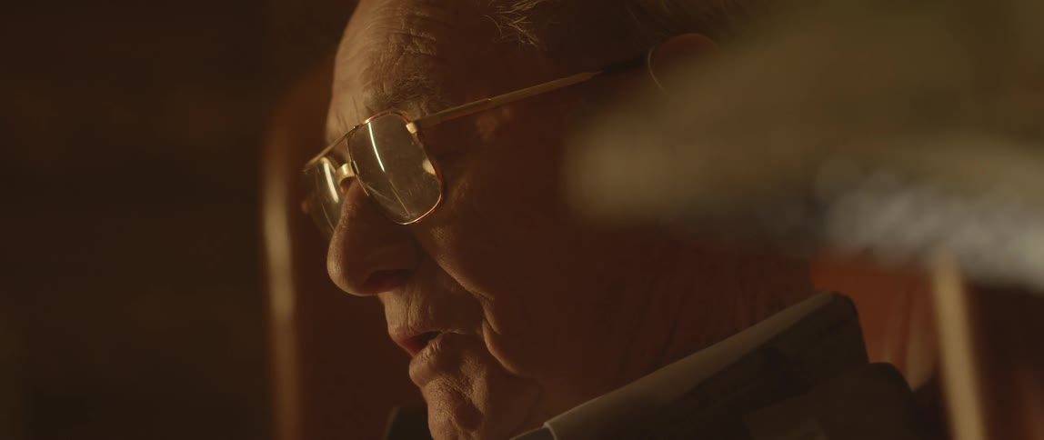 An elderly man reads a book sitting in a leather chair