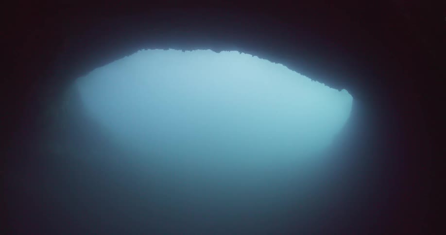 Light shines through murky water illuminating mouth of under water cave