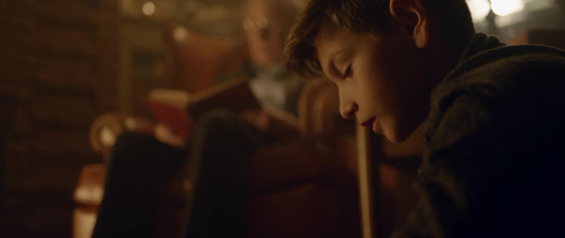 A young boy plays a toy near an elderly man reading a book