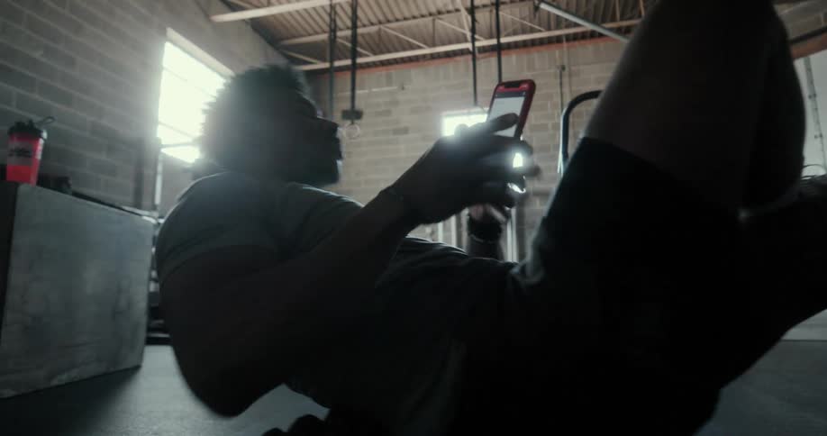 A man in a room looking at a smartphone and exercising with a wall and windows in the background