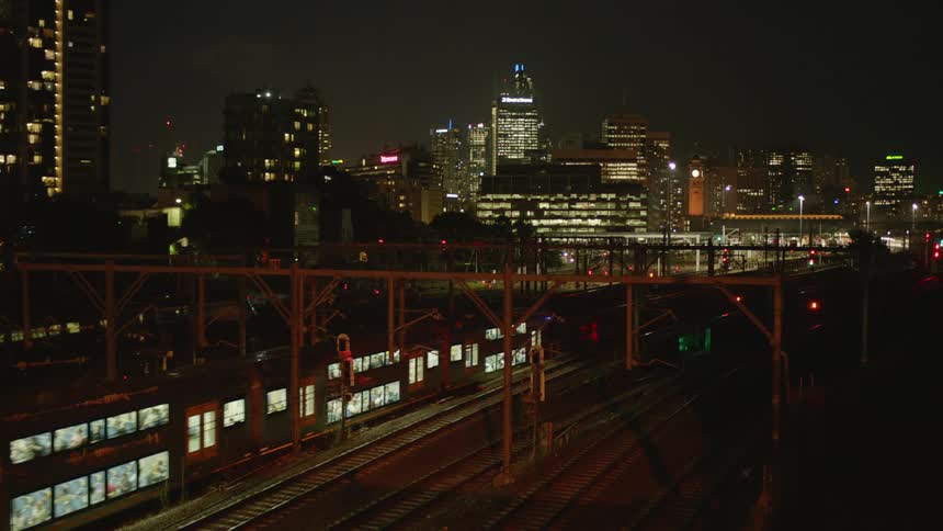 Passenger train windows glow at night with a city skyline behind