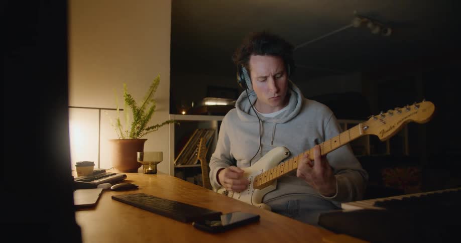 A man is playing guitar at his desk