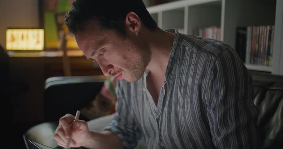 A man in a room using a stylus and tablet with a wall in the background