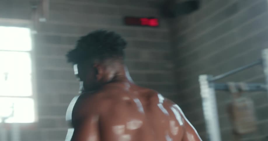 Bare chested man drops from rope he was climbing and walks across gym