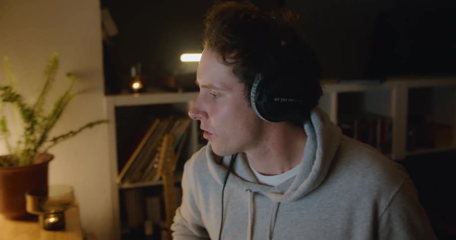 A male guitarist sits in front of his laptop computer and listens to a recording of his music