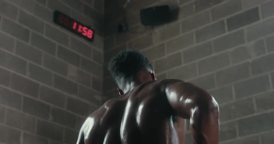 A man covered in sweat wipes his face with a towel and attempts to catch his breath in a gym during the day