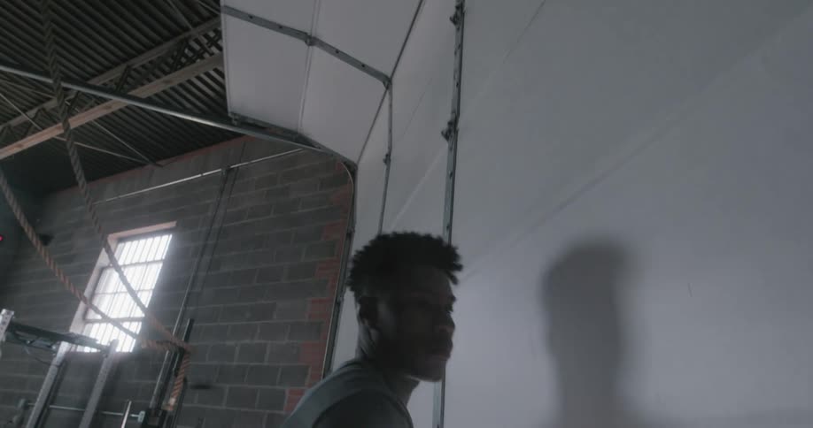 A man rolls up a garage door in a gym
