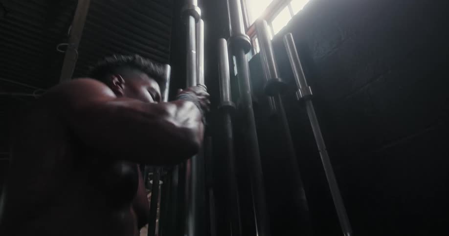 A muscular man removes a bare barbell from a rack in a gym and carries it away