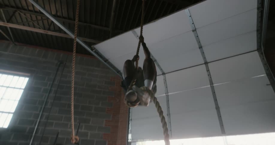 A man climbs up a rope in a garage gym