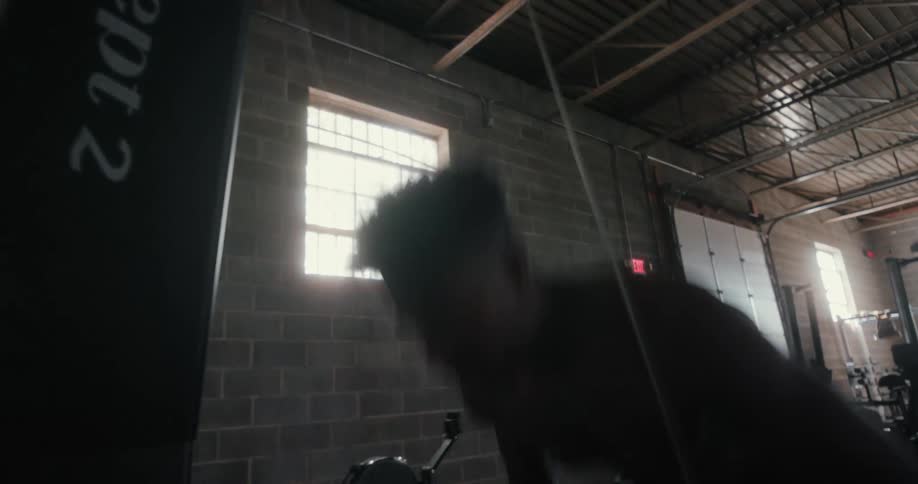 Strong energetic shirtless muscular young man excercising in a dimly lit gym