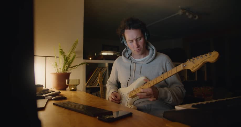 A man uses the track pad on a laptop while playing guitar
