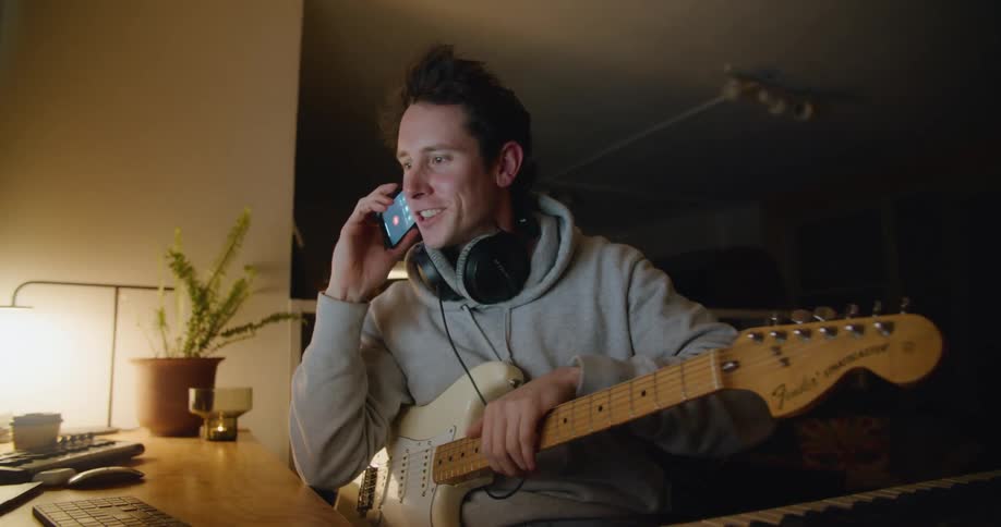A man in a room with headphones using a smartphone with a wall in the background