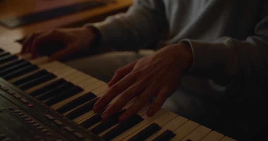 Musician plays keyboard occasionally checking laptop screen as he bobs his head