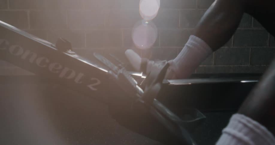 A shirtless man walks over to a rowing machine gets on and starts to pull